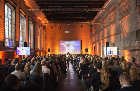 En fullsatt sal med mennesker foran en scene. Hallen på DOGA. Seminar.