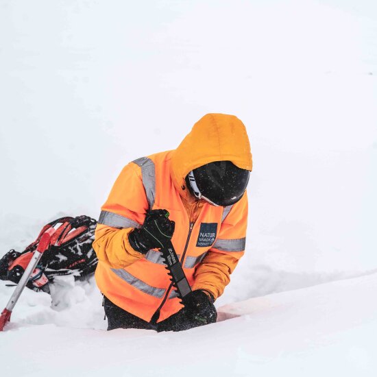 Bildet viser en person i dyp snø som sager i snøen med snøsag.