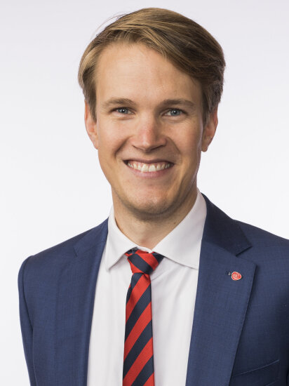 Portrett av Torstein Tvedt Solberg i blå dressjakke med Arbeiderpartiet-pin på jakkeslaget.