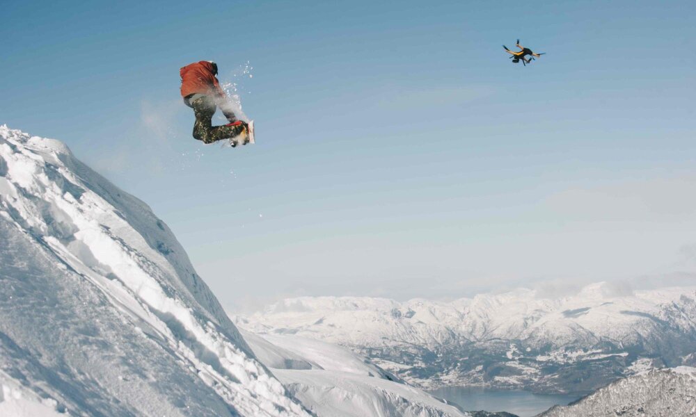 Person hopper på snowboard og følges av drone. 