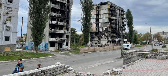 Bildet viser to utbombede boligblokker i Ukraina. I forgrunnen en voksen mann og to barn.